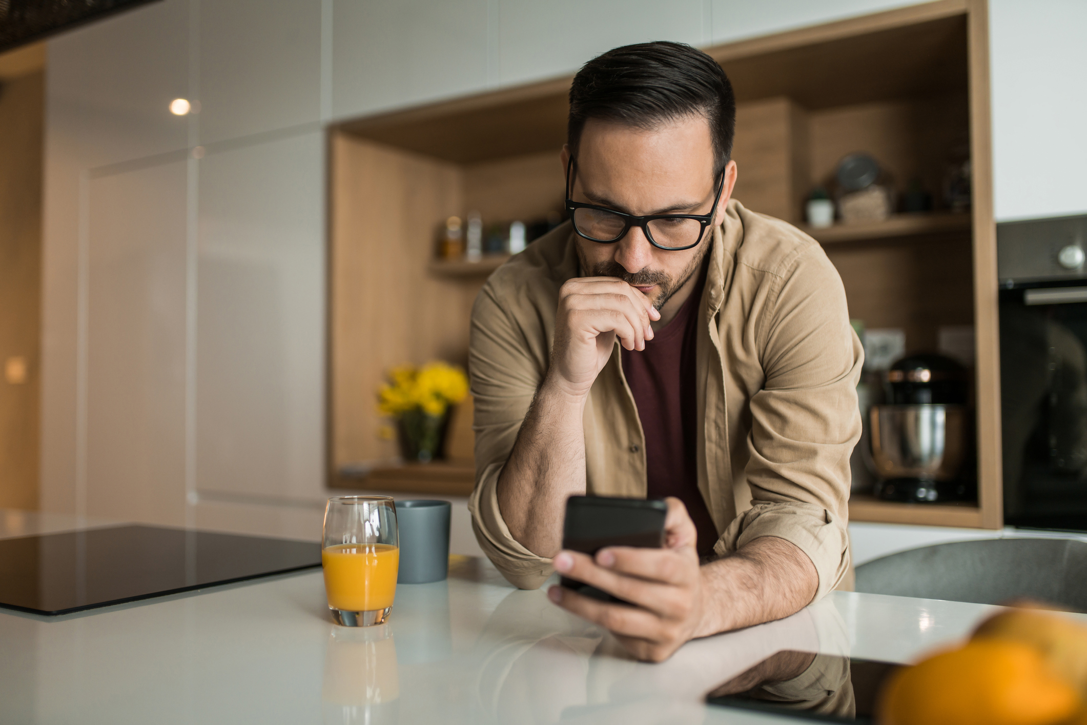 Serious young man using his cell phone on kitchen counter at home.