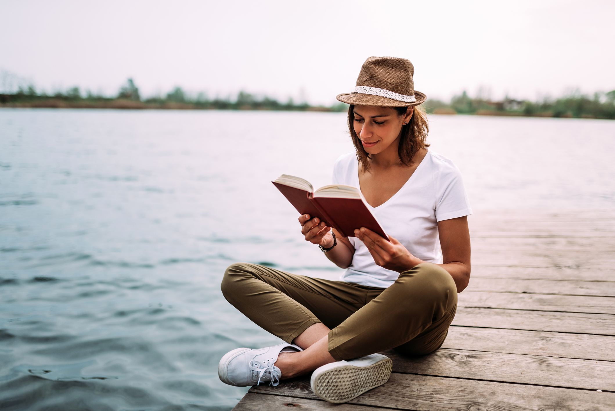 Gorgeous woman sitting on wooden pier and reading book.