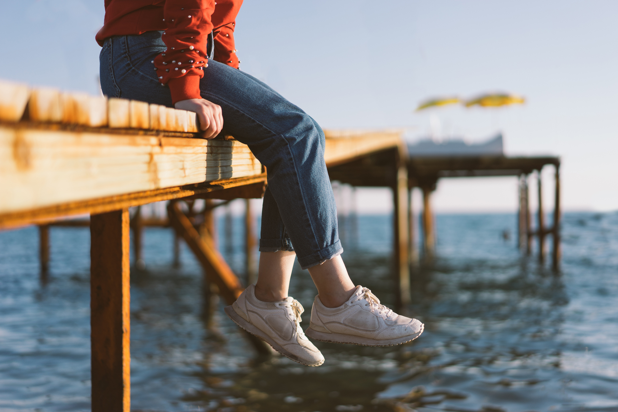 Woman's feet dangle from wooden wharf, above sea