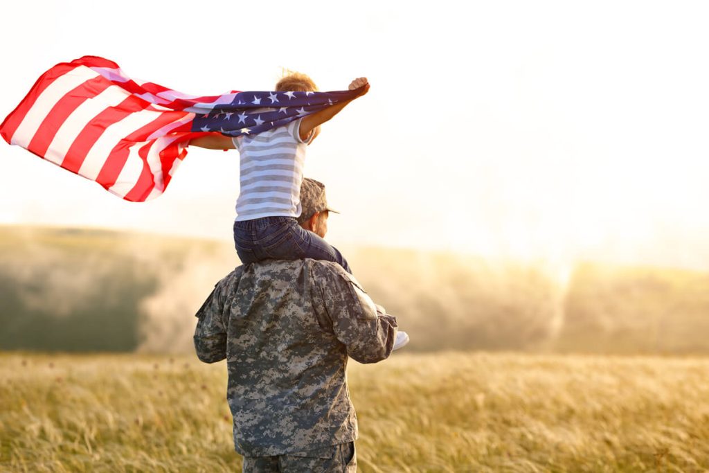 A soldier carrying a child on his shoulders holding an American flag