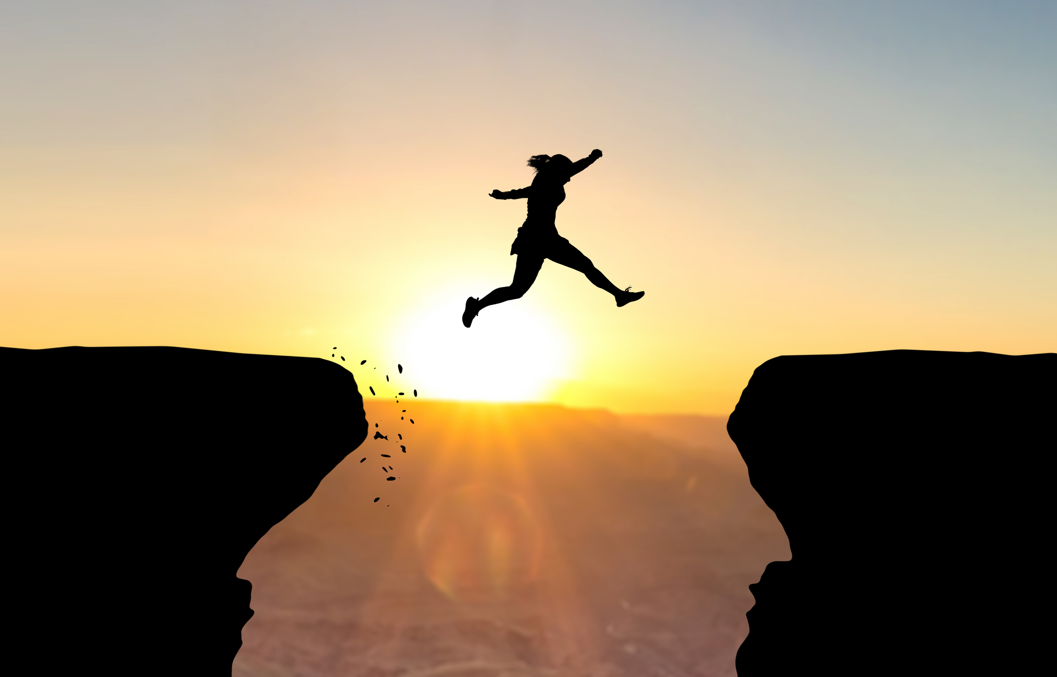 Woman jumping over abyss in fornt of sunset