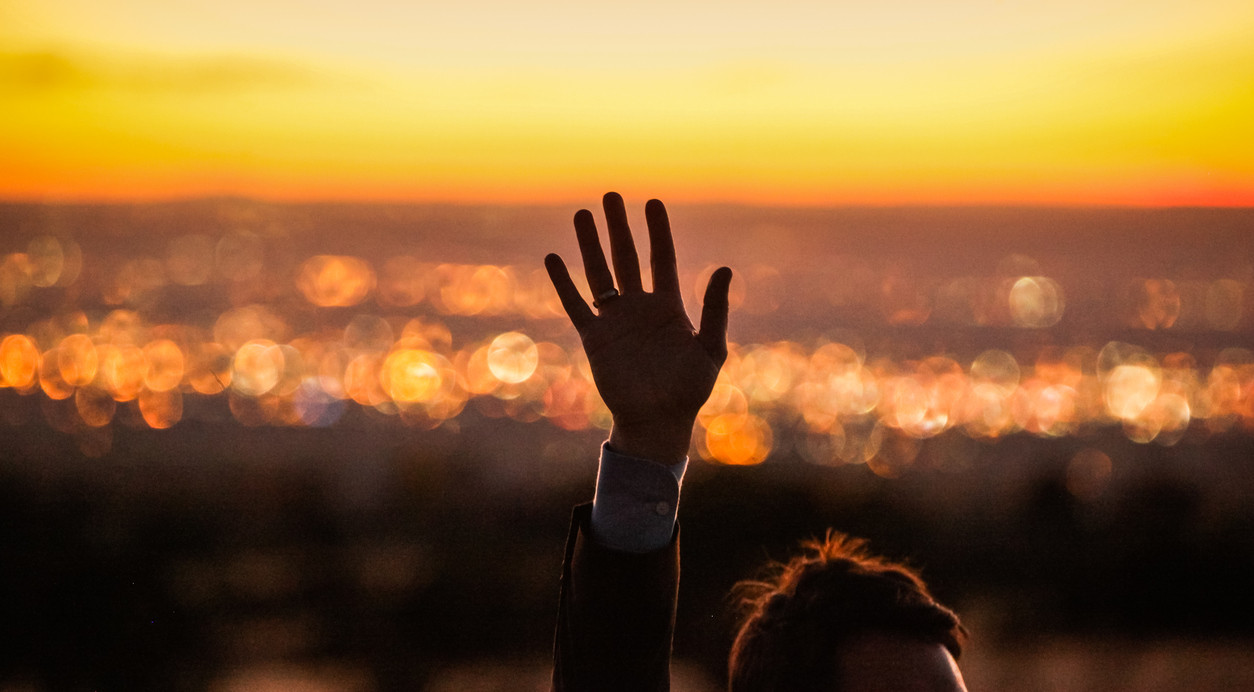 A raised hand against the background of the setting sun over the sea