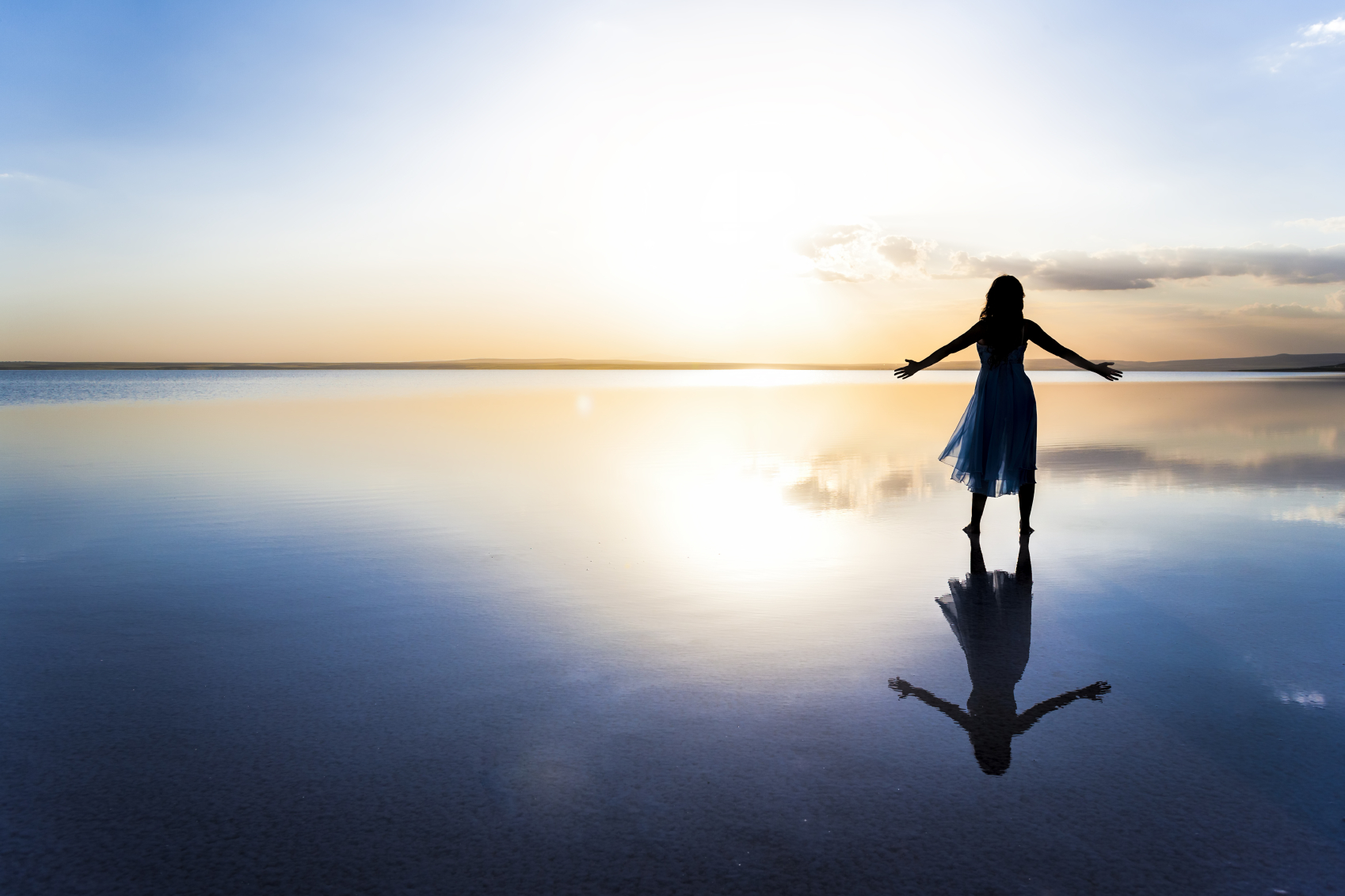 A woman standing in the middle of a lake with the rising sun in the background