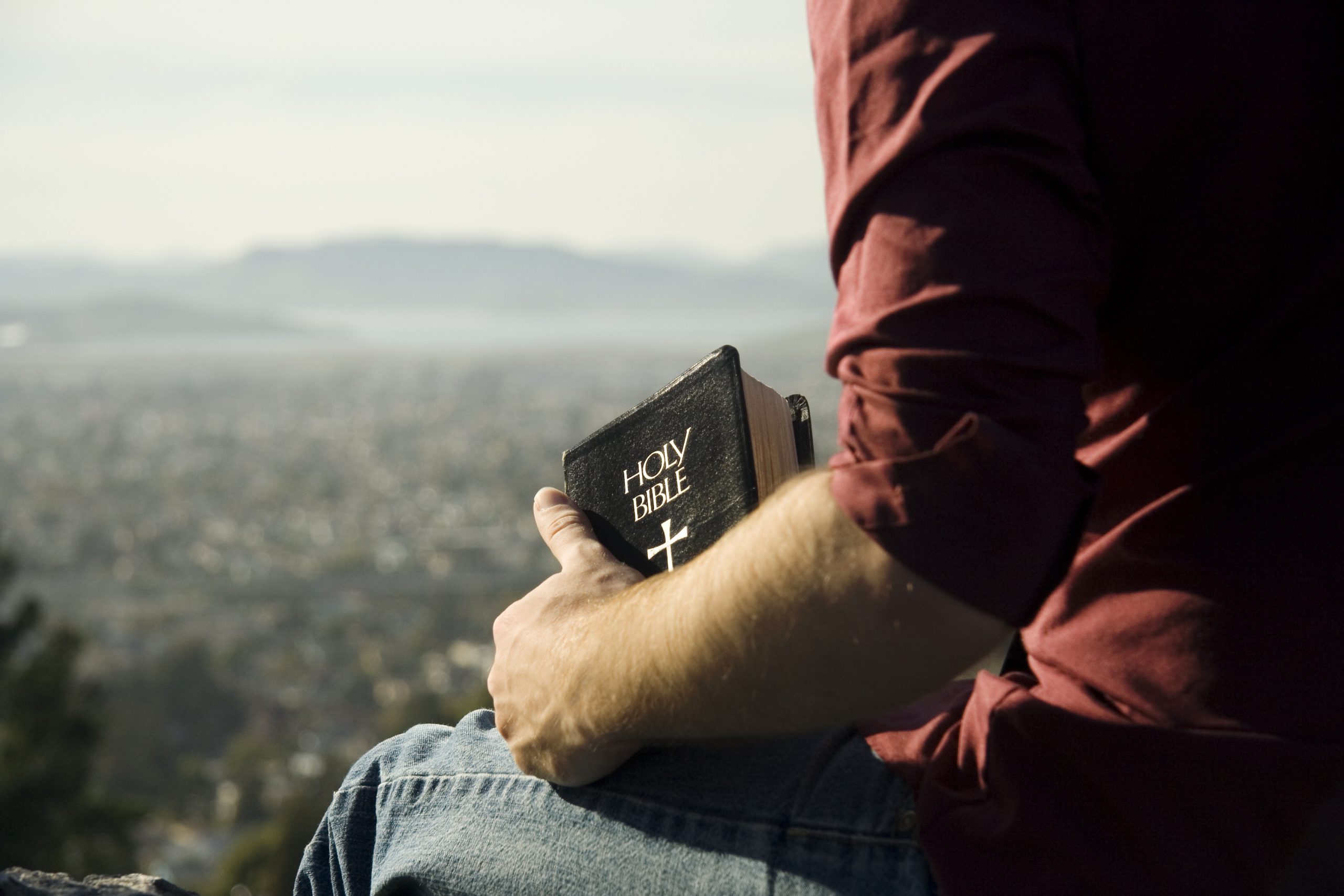 Man thinking on a cliff with the bible