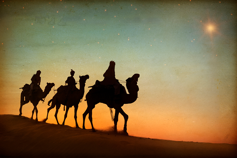 Three wise men traveling through the desert on camels against the background of the sunset