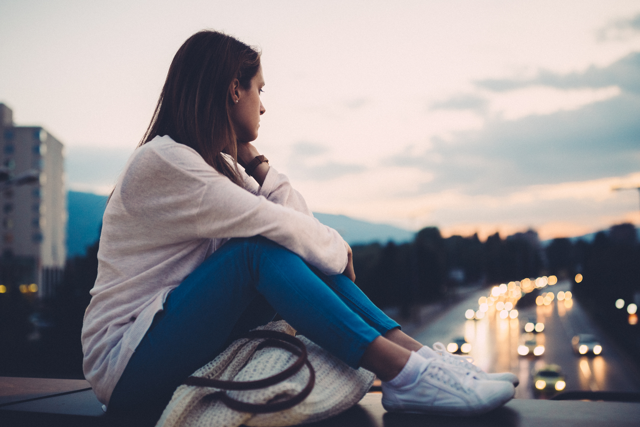 Unhappy woman sitting at the bridge and looking at the cityscape