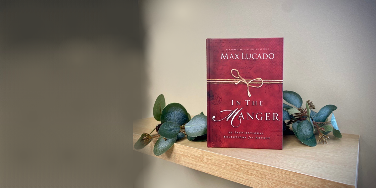 Max Lucado's book In the Manger. It has a red cover and is upright on a shelf surrounded by pale green eucalyptus leaves