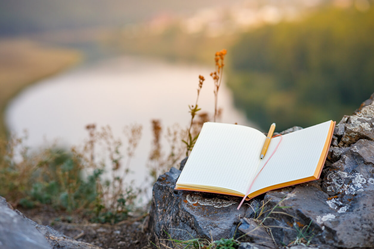 Open notebook on a rock. It's above a river with large bluffs overlooking it.